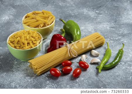 Raw pasta with fresh vegetables on a gray background Raw pasta with fresh vegetables on a gray background 73260333