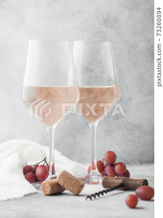 Glasses of rose pink summer wine with corks, grapes and corkscrew on light background. 73260894