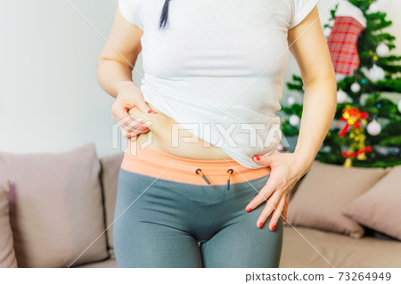 Woman showing fat on front side of waist.New Year's weight loss challenge concept Woman showing fat on front side of waist.New Year's weight loss challenge concept 73264949