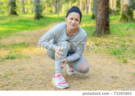 Female runner with injured and painful leg on park path Female runner with injured and painful leg on park path 73265865