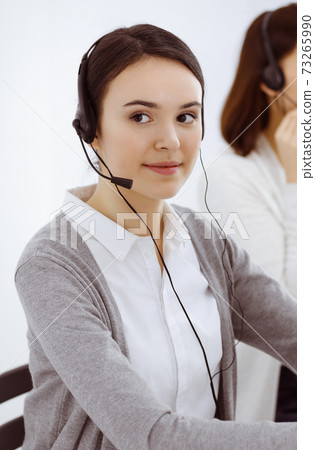 Call center. Casual dressed woman working in headset with diverse colleagues at office. Business concept 73265990