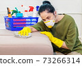 Woman in protective face mask cleaning sofa 73266314