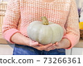 Woman holding green pumpkin in kitchen 73266361