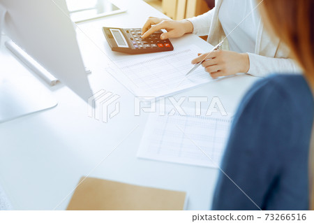 Accountant checking financial statement or counting by calculator income for tax form, hands close-up. Business woman sitting and working with colleague at the desk in office. Audit concept Accountant checking financial statement or counting by calculator income for tax form, hands close-up. Business woman sitting and working with colleague at the desk in office. Audit concept 73266516