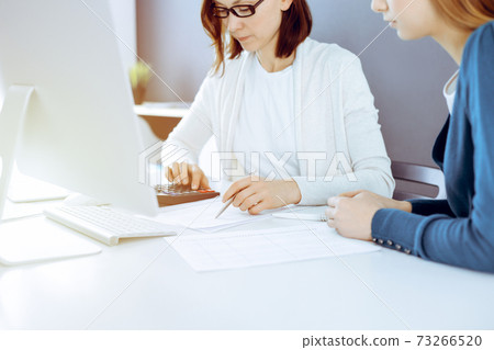Accountant checking financial statement or counting by calculator income for tax form, hands close-up. Business woman sitting and working with colleague at the desk in office. Audit concept Accountant checking financial statement or counting by calculator income for tax form, hands close-up. Business woman sitting and working with colleague at the desk in office. Audit concept 73266520