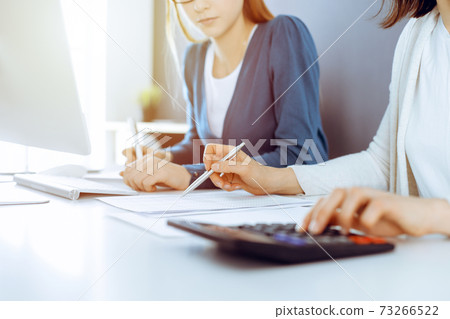 Accountant checking financial statement or counting by calculator income for tax form, hands close-up. Business woman sitting and working with colleague at the desk in office. Audit concept 73266522