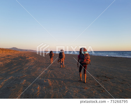 Tourists with backpacks are walking along the beach 73268795