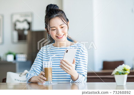 A young woman watching a smartphone at a cafe 73268892