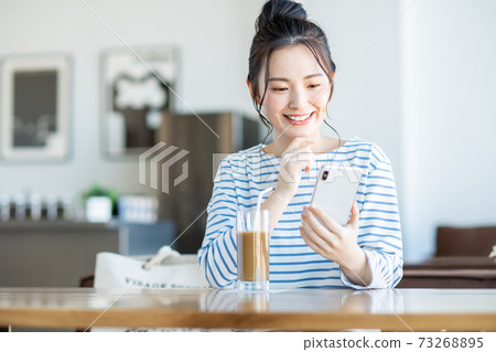 一個年輕的女人，看著一家咖啡館的智能手機 73268895