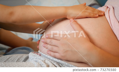 Closup of little children hand stroking and caressing big belly of pregnant mother. Elder child love and cares of unborn future baby 73270380