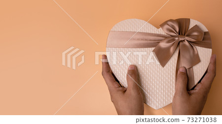 Love and Valentines Day Concept. Hands holding a Golden Heart Shape Gift Box. Top View Love and Valentines Day Concept. Hands holding a Golden Heart Shape Gift Box. Top View 73271038