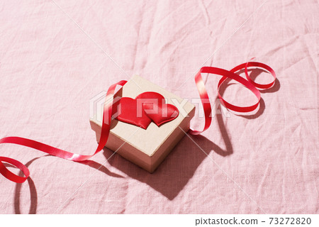 Valentines day festive card with gift box decorated with red hearts and ribbon on the pink bed sheet Valentines day festive card with gift box decorated with red hearts and ribbon on the pink bed sheet 73272820