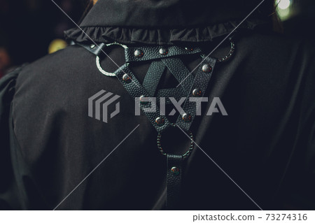 Back shot of a lady with curly hair in a white sleeveless blouse and a black harness made of textile straps with rivets and plastic hooks. The girl is posing. Back shot of a lady with curly hair in a white sleeveless blouse and a black harness made of textile straps with rivets and plastic hooks. The girl is posing. 73274316