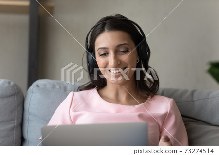 Happy ethnic woman in earphones talk on laptop 73274514