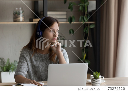 Pensive woman in headphones work on laptop thinking 73274520