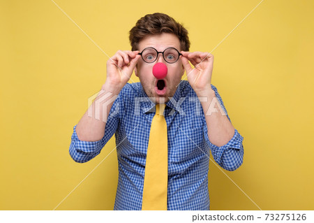 Surprised handsome man dressed as clown looking through glasses. 73275126