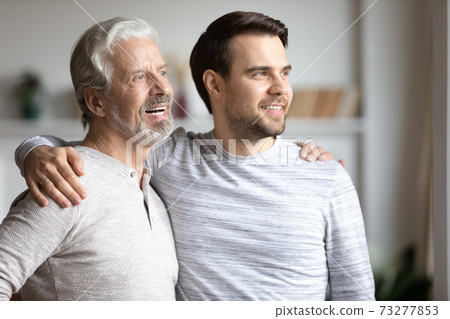 Happy adult son and senior father look in distance Happy adult son and senior father look in distance 73277853