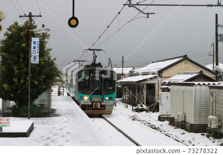 125 series train arriving at Tomura station in the snowy landscape 73278322