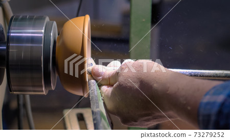 Carpenter using chisel for shaping wood piece on lathe - side view 73279252