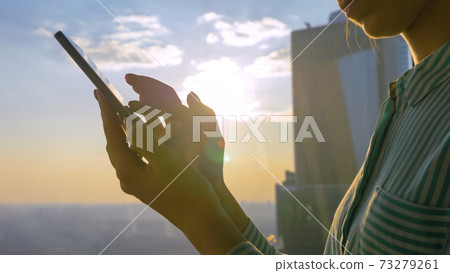 Woman using smartphone against sunset cityscape through window of skyscraper Woman using smartphone against sunset cityscape through window of skyscraper 73279261