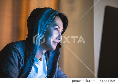 A man wearing a hood and using a computer at night A man wearing a hood and using a computer at night 73284106
