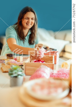 Young woman placing handmade organic bath supplies into bridesmaid gift box set. 73287742