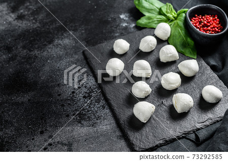 Mini mozzarella cheese balls on a stone Board with Basil leaves and pink pepper. black background. Top view. Copy space Mini mozzarella cheese balls on a stone Board with Basil leaves and pink pepper. black background. Top view. Copy space 73292585