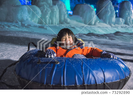 Cute Asian child playing sledge in snow festival on night winter Cute Asian child playing sledge in snow festival on night winter 73292890