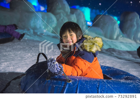 Cute Asian child playing sledge in snow festival on night winter Cute Asian child playing sledge in snow festival on night winter 73292891