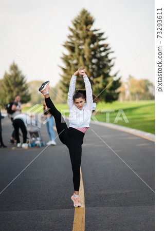 Woman in sport outfit on the road doing doing splits standing. Woman in sport outfit on the road doing doing splits standing. 73293611