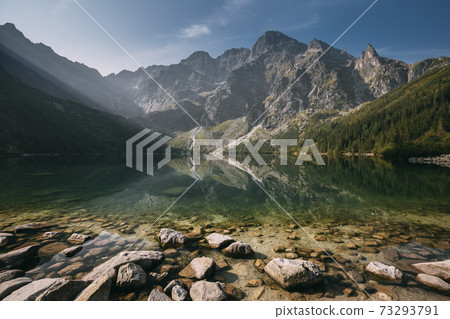 Tatra National Park, Poland. Famous Mountains Lake Morskie Oko Or Sea Eye Lake In Summer Morning Sunrise. Beautiful Sunrays Above Tatras Lake Landscape. Tatra National Park, Poland. Famous Mountains Lake Morskie Oko Or Sea Eye Lake In Summer Morning Sunrise. Beautiful Sunrays Above Tatras Lake Landscape. 73293791