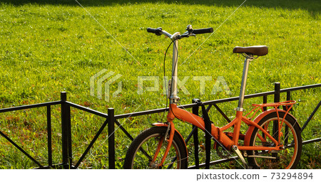 Walking compact city bike on green grass background with copy space. City tourism and bike rental service 73294894