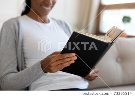 Happy young african ethnicity woman reading favorite book. 73295514