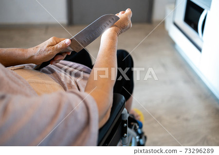 Sick senior woman suffer from depression,debilitating diseases,hopeless,despair from cancer and disability,a crying old people sitting in a wheelchair and holding a knife is about to commit suicide Sick senior woman suffer from depression,debilitating diseases,hopeless,despair from cancer and disability,a crying old people sitting in a wheelchair and holding a knife is about to commit suicide 73296289