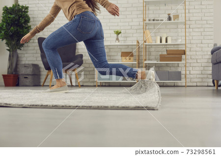 Clumsy woman stumbles on the rug in the living-room and falls down on the floor 73298561
