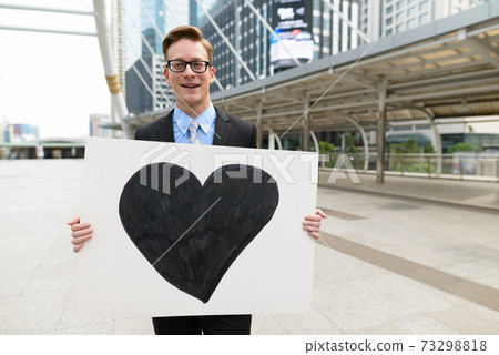 Happy young handsome blond businessman holding heart sign in the city outdoors 73298818