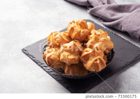 Profiteroles with custard and powdered sugar on a plate. Concrete grey table. Copy space. 73300175