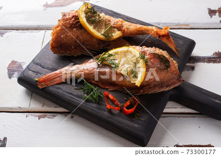Baked sea bass with tomato pepper lemon and herbs on wooden Board for filing on white wooden background. Perch fish cooked in the oven. 73300177
