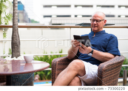 Happy senior handsome tourist man using phone and relaxing with nature outdoors Happy senior handsome tourist man using phone and relaxing with nature outdoors 73300220