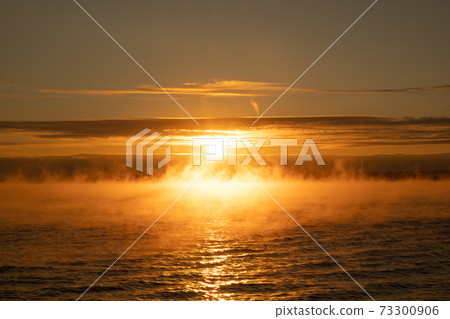Fog over the sea at sunset. Bright yellow light. The sun against the sky. Water evaporation and heat Fog over the sea at sunset. Bright yellow light. The sun against the sky. Water evaporation and heat 73300906
