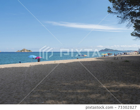 view of sand beach Spiaggia di Santa Maria Navarrese, sea with colorful beach umbrella and sunbeds and view of Arbatax penisula. Summer sunny day, Sardinia, Italy view of sand beach Spiaggia di Santa Maria Navarrese, sea with colorful beach umbrella and sunbeds and view of Arbatax penisula. Summer sunny day, Sardinia, Italy 73302827