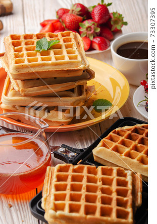 Belgian waffles on cast skillet with stacked ones and syrup jug  aside 73307395