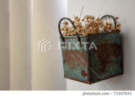 Bunch of tinny artificial flowers, hay colored, inside a blue metal box, very old and rusted, hanging on the wall Bunch of tinny artificial flowers, hay colored, inside a blue metal box, very old and rusted, hanging on the wall 73307641