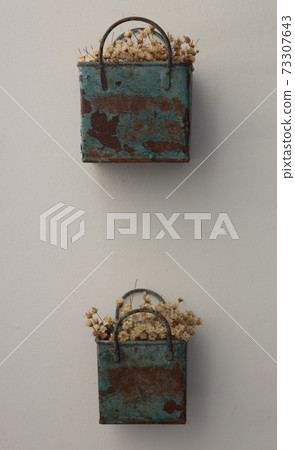 Bunch of tinny artificial flowers, hay colored, inside a blue metal box, very old and rusted, hanging on the wall 73307643