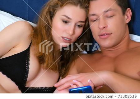 Portrait young couple in underwear in bed is watching something in smartphone. 73308539