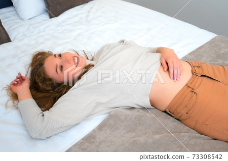 Tired happy young woman is lying on bed in hotel after hard road. Tired happy young woman is lying on bed in hotel after hard road. 73308542