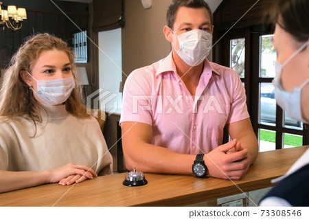 Woman receptionist on reception at the hotel with couple of guests in masks. Woman receptionist on reception at the hotel with couple of guests in masks. 73308546