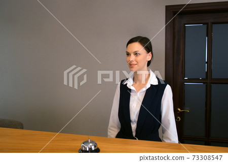 Woman receptionist on reception at the hotel with a bell on a wooden table. Woman receptionist on reception at the hotel with a bell on a wooden table. 73308547