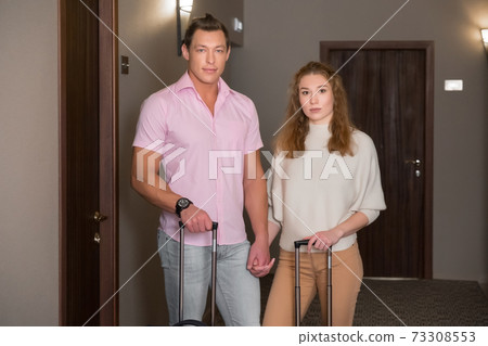 Young family man and woman with suitcases near their room in hotel in corridor. Young family man and woman with suitcases near their room in hotel in corridor. 73308553