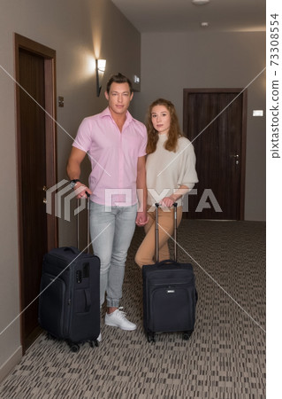 Young family man and woman with suitcases near their room in hotel in corridor. Young family man and woman with suitcases near their room in hotel in corridor. 73308554